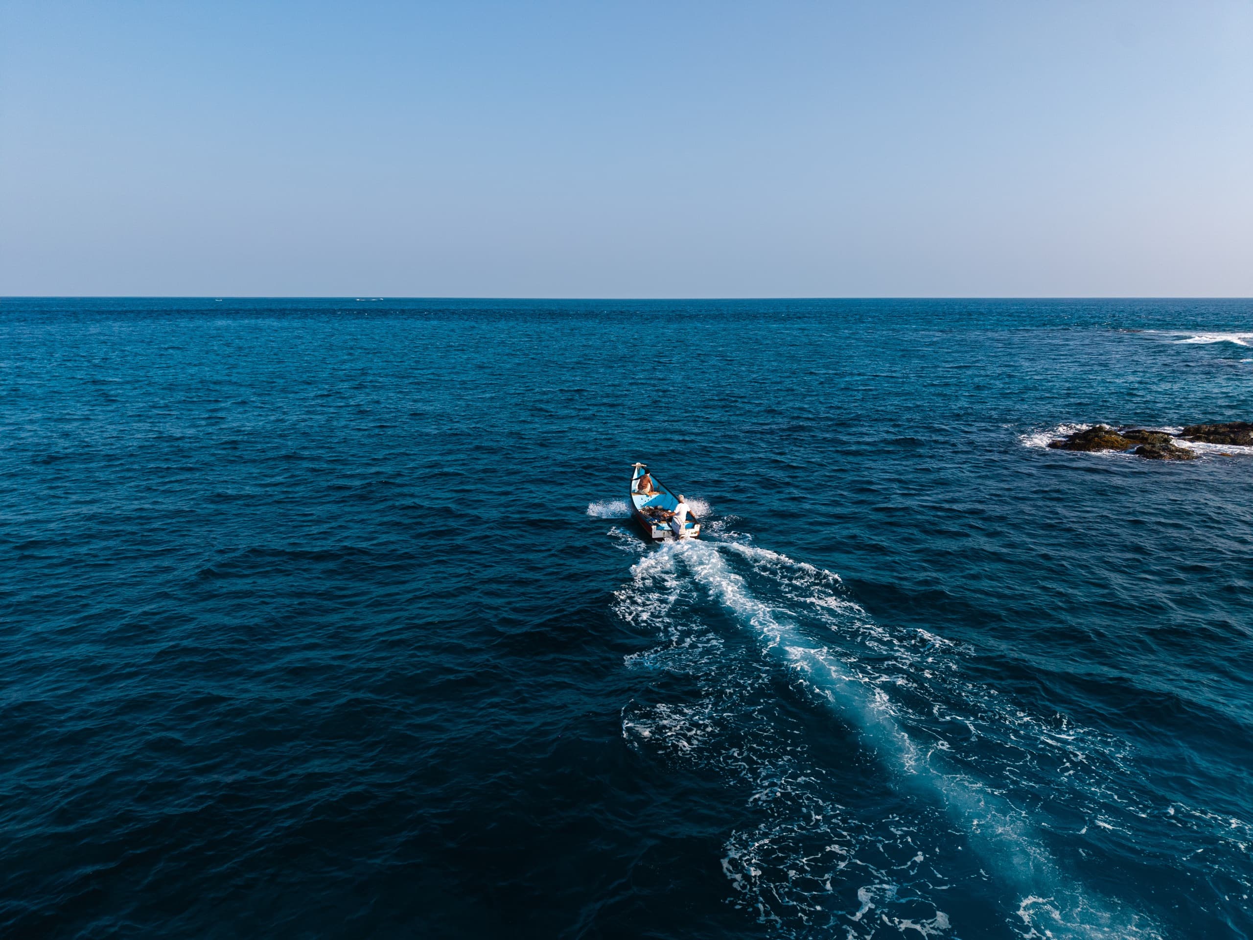 A small fishing boat cutting a white wake across deep blue water