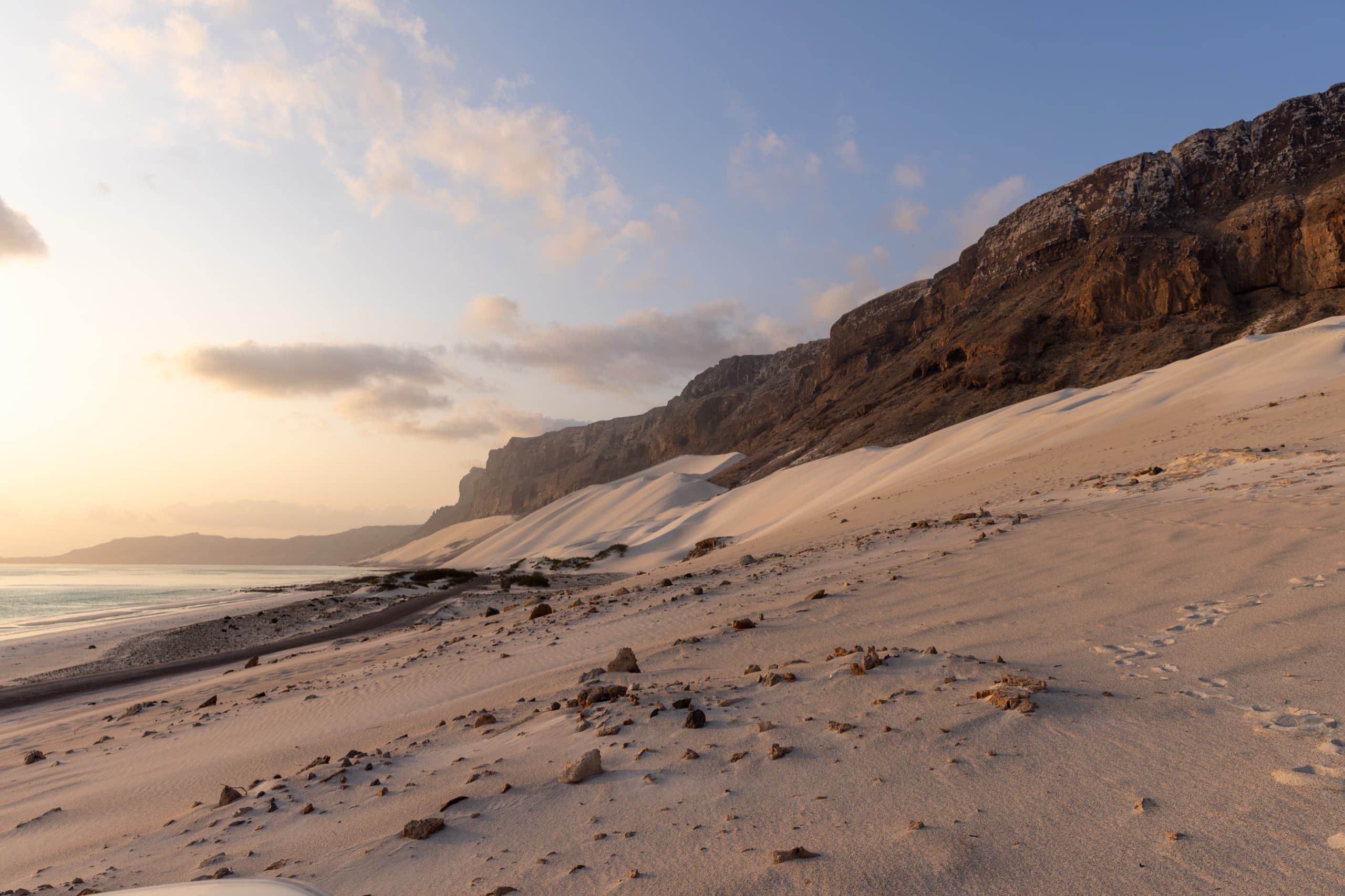 White sand dunes climbing a dark cliff down to the sea at golden hour
